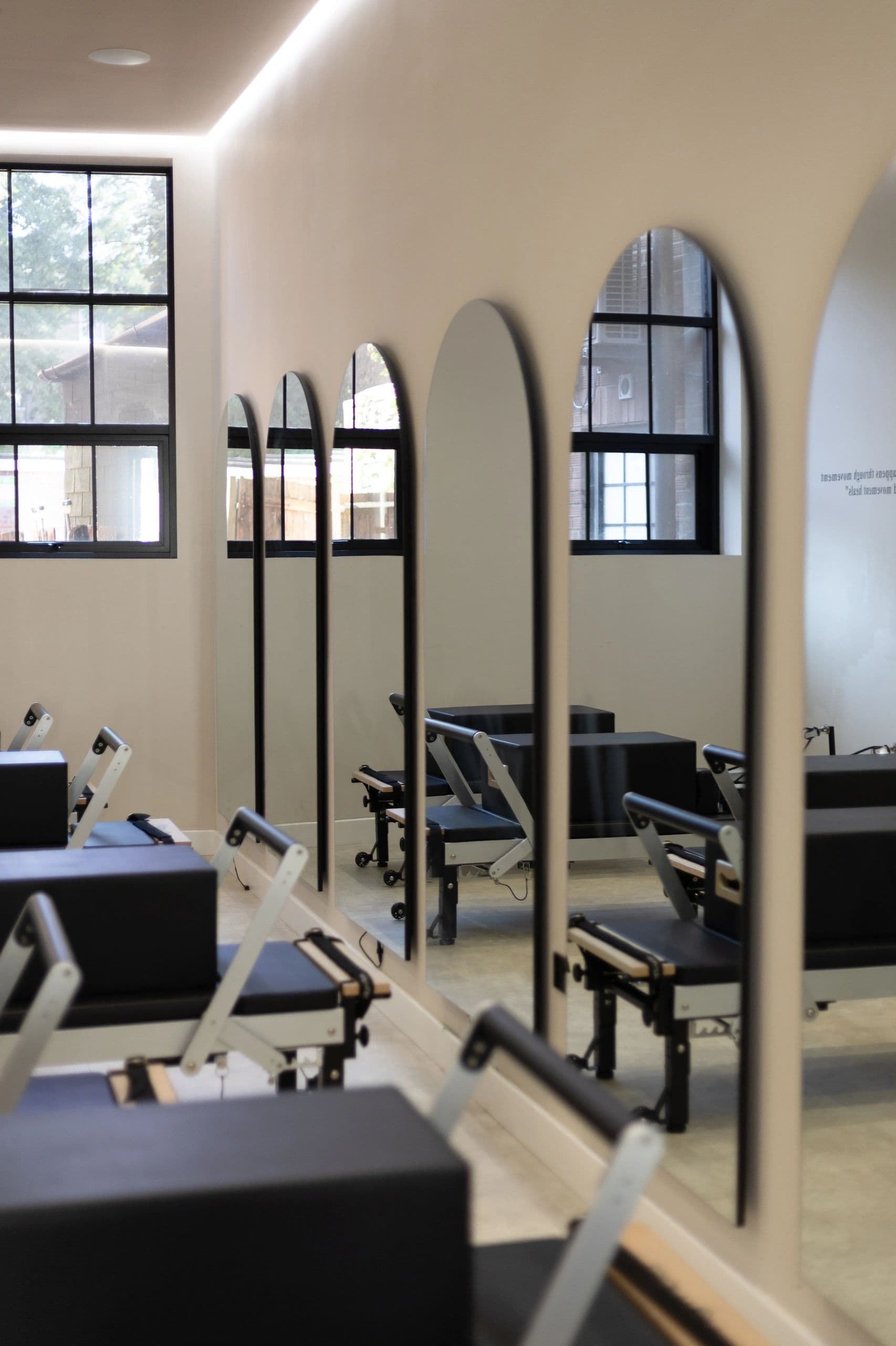The studio interior, arched mirrors along a cream wall above the reformers